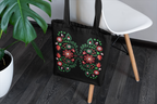 Black tote bag with floral design on a wooden floor next to a white chair and plant.