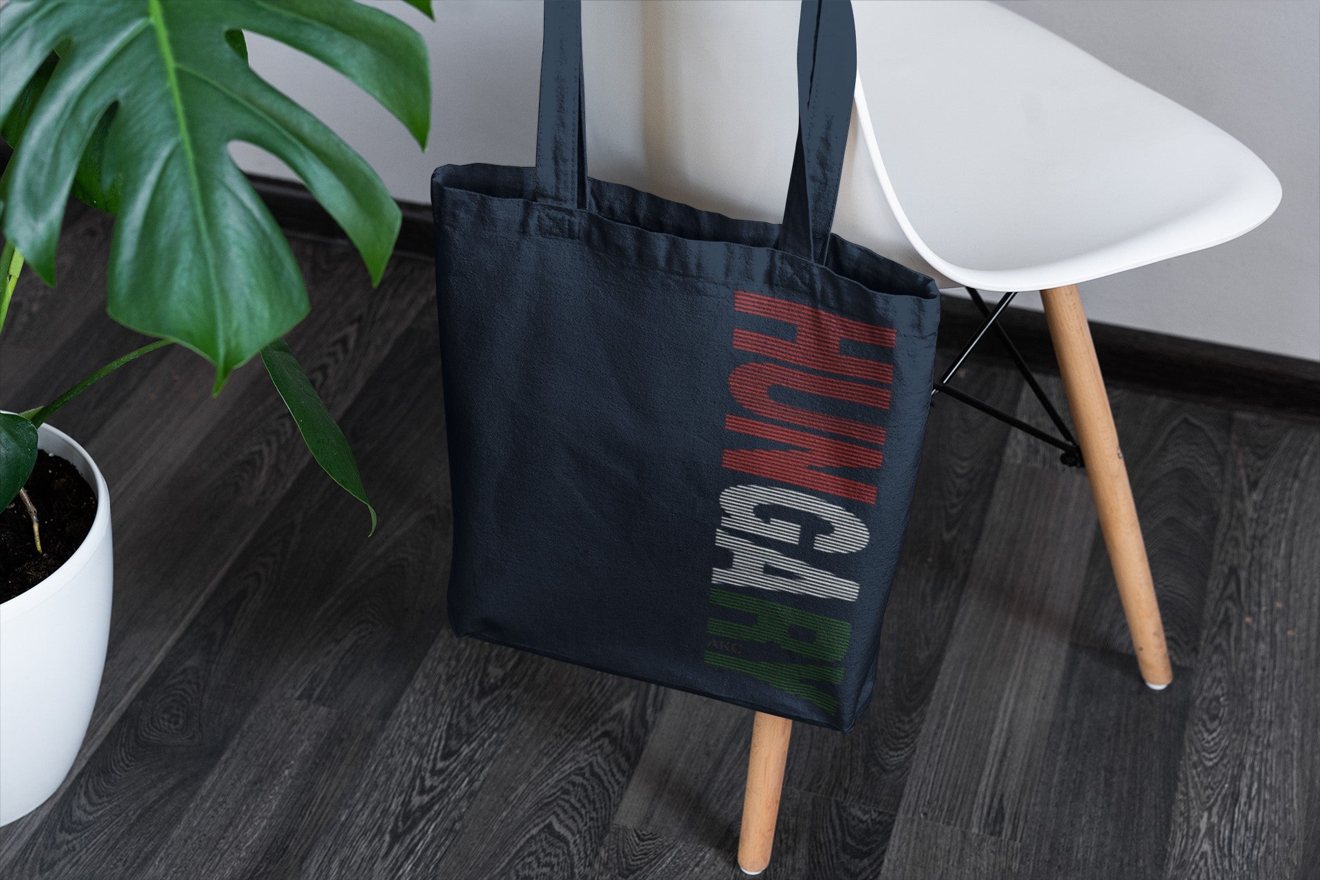 Black tote bag with 'HUNGA' branding on a wooden floor next to a white chair and plant.