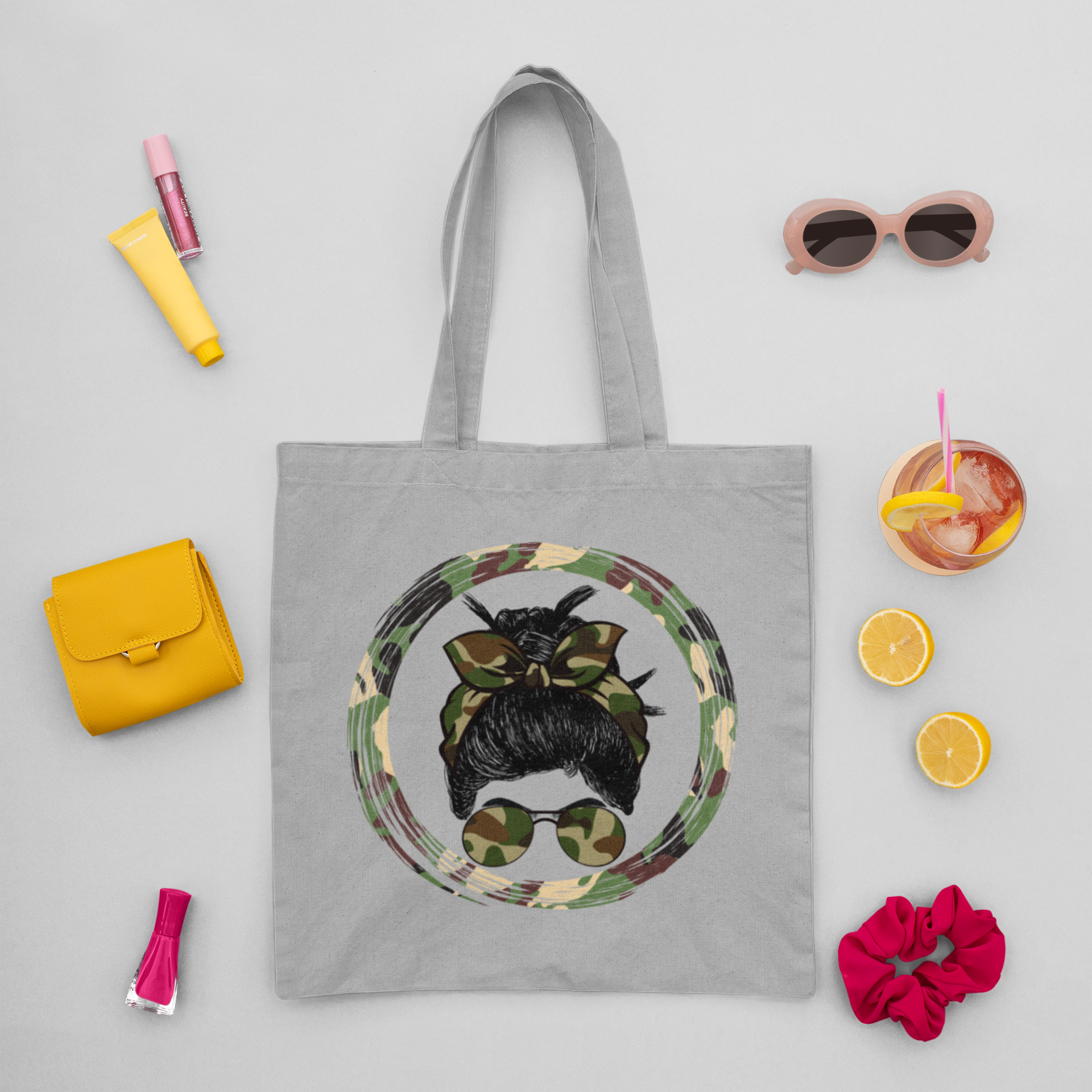 Gray tote bag with a design of a person with a bun wearing sunglasses, surrounded by small items on a light gray background.