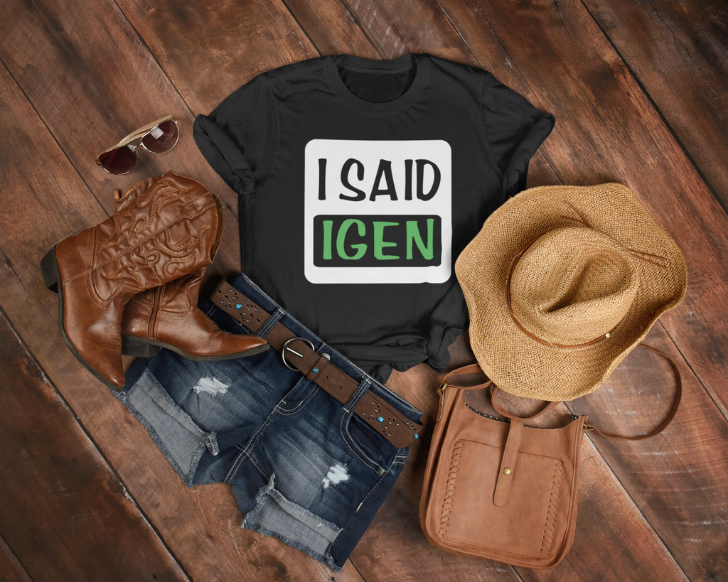 Black t-shirt with 'I SAID IGEN' text, cowboy boots, hat, and purse on a wooden surface