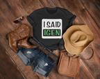 Black t-shirt with 'I SAID IGEN' text, cowboy boots, hat, and purse on a wooden surface