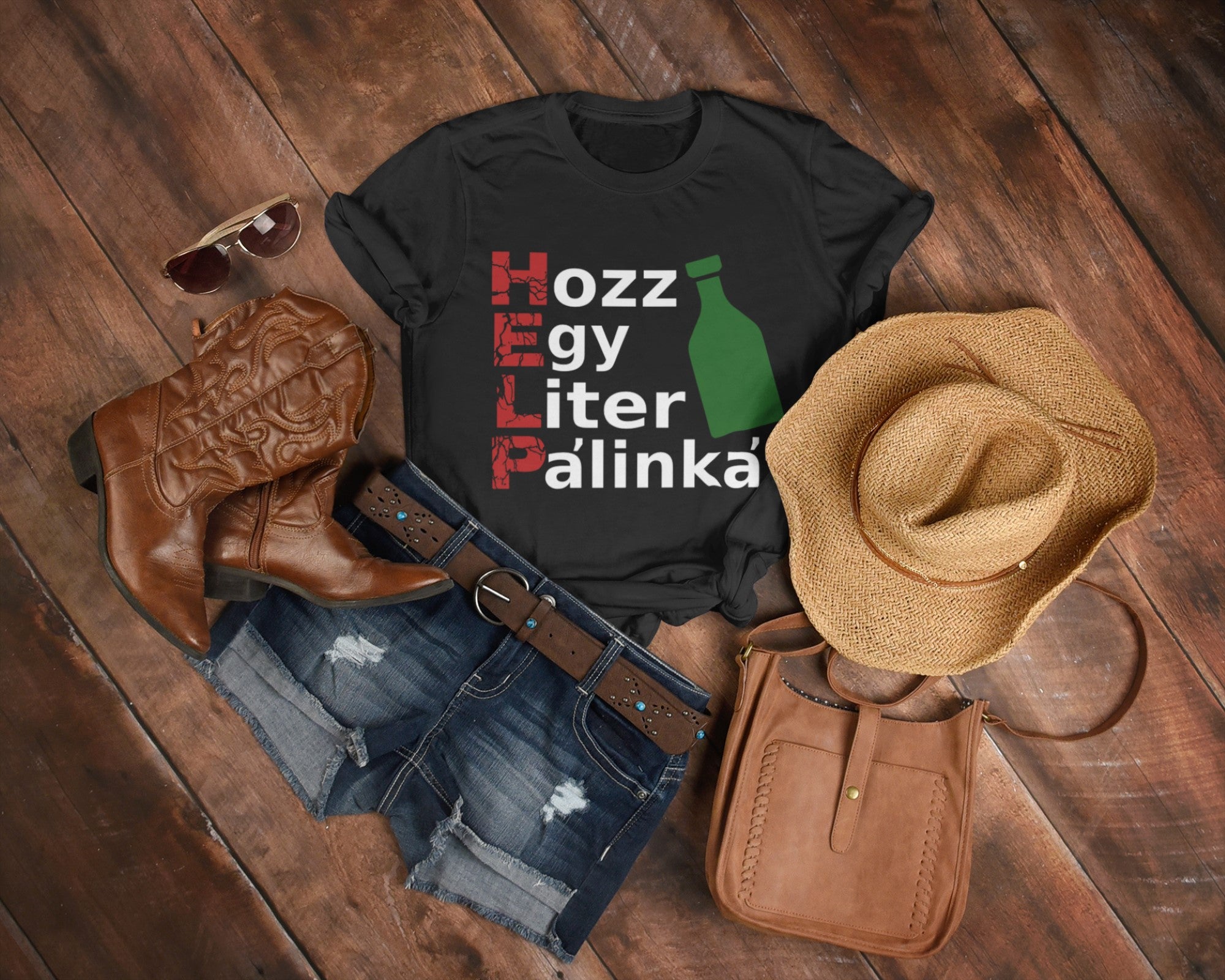 Black t-shirt with text and graphics, paired with cowboy boots, shorts, hat, and purse on a wooden surface.