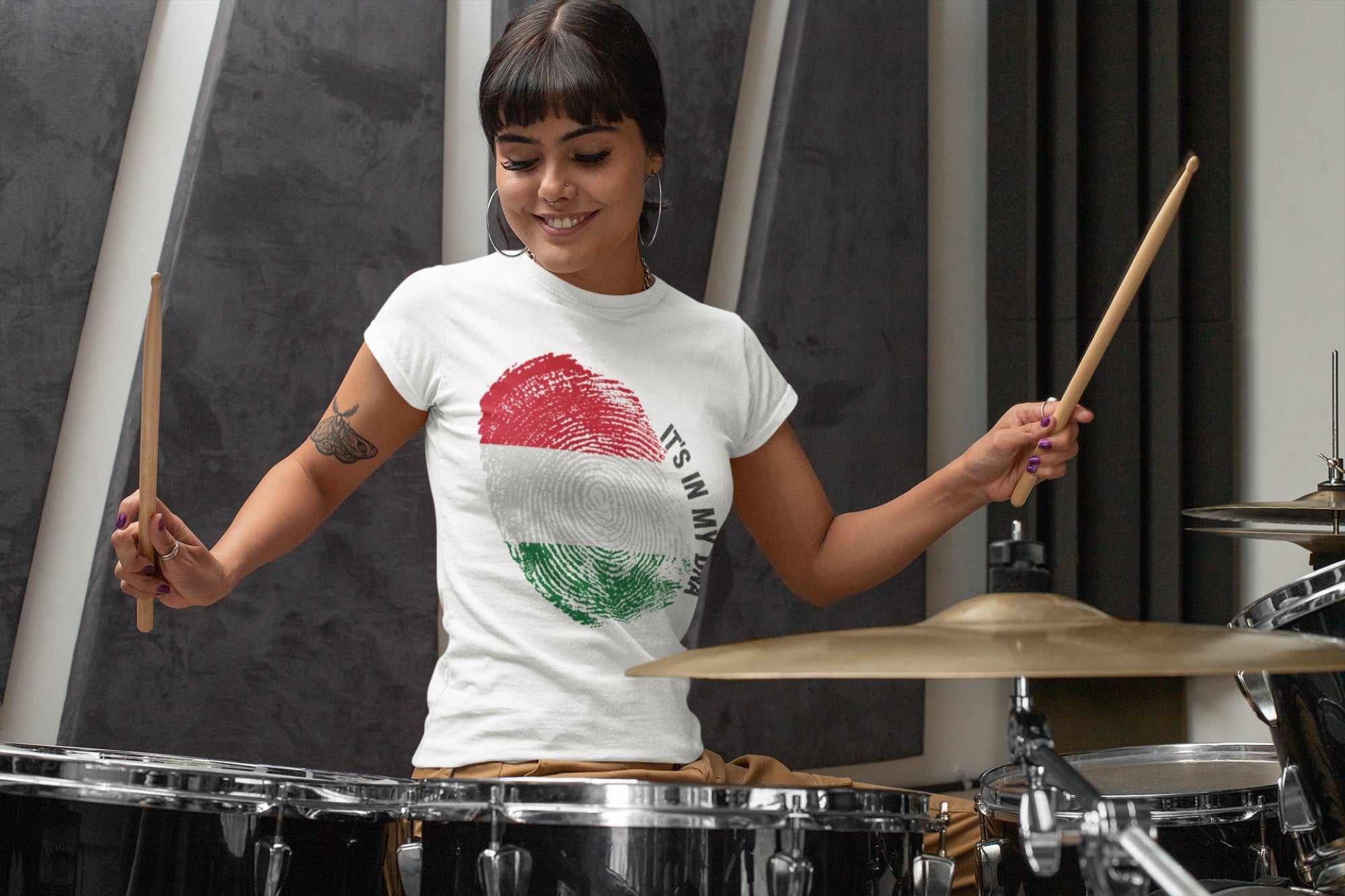 Woman playing drums wearing a white t-shirt with a colorful logo.