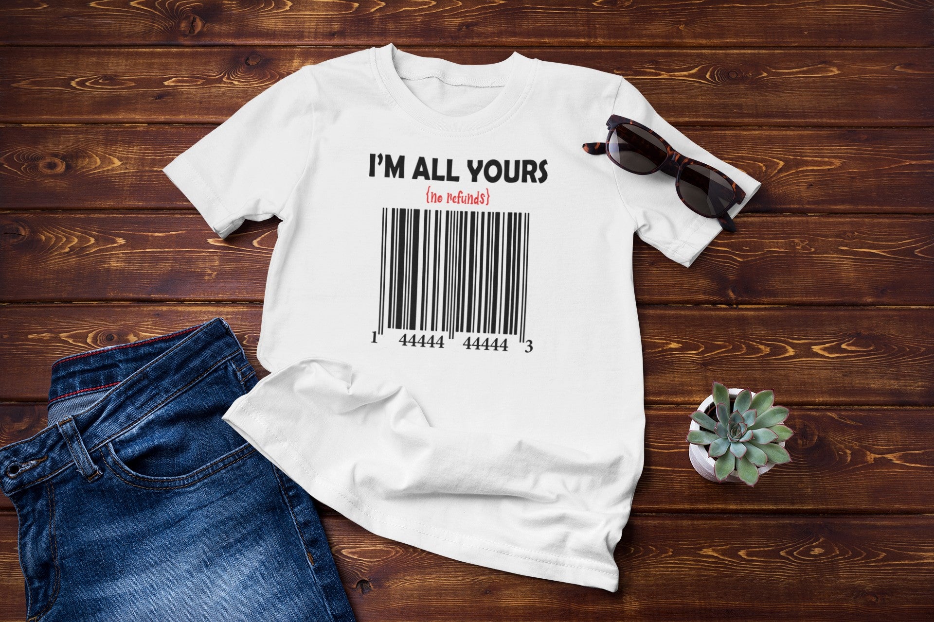 White t-shirt with 'I'm All Yours' text and barcode design on a wooden surface with jeans and sunglasses.