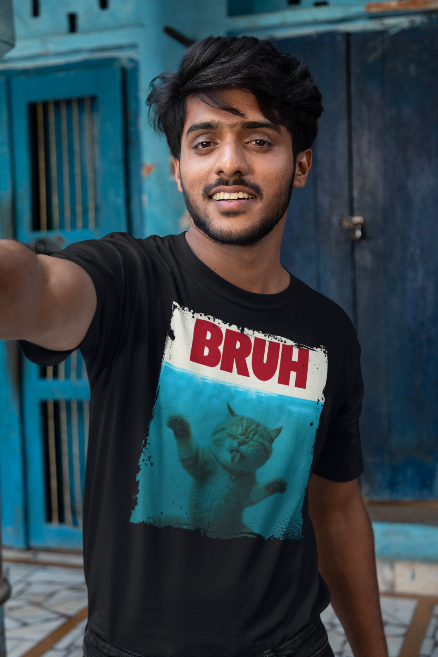 Person wearing a black t-shirt with a graphic design and text, standing in front of a blue door.