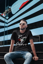 A man wearing a black graphic t-shirt with the text 'Rise Above' and a red, white, and green design, sitting on outdoor steps in front of a modern glass building.