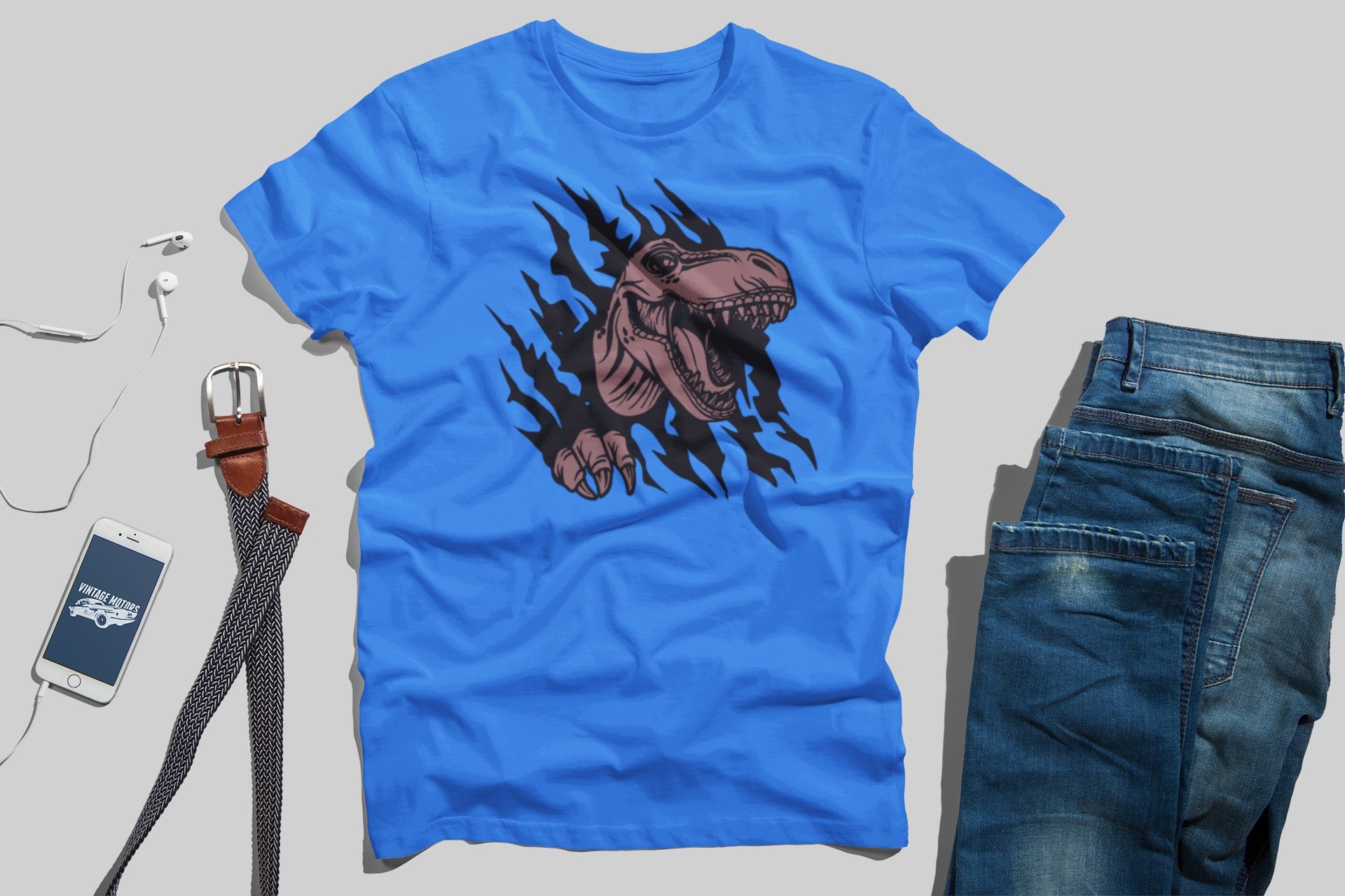 Blue t-shirt with dinosaur graphic, jeans, phone, and belt on a light gray background
