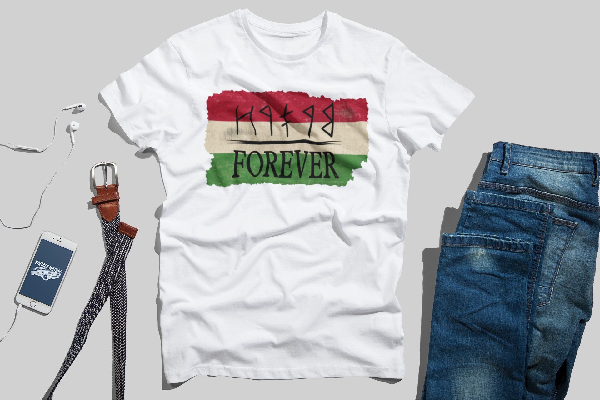 White t-shirt with colorful graphic design, blue jeans, smartphone, and belt on a gray background