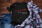 Black t-shirt with 'C.R.E.A.M. Cash Rules Everything Around Me' text on a wooden surface with jeans and a plaid shirt.