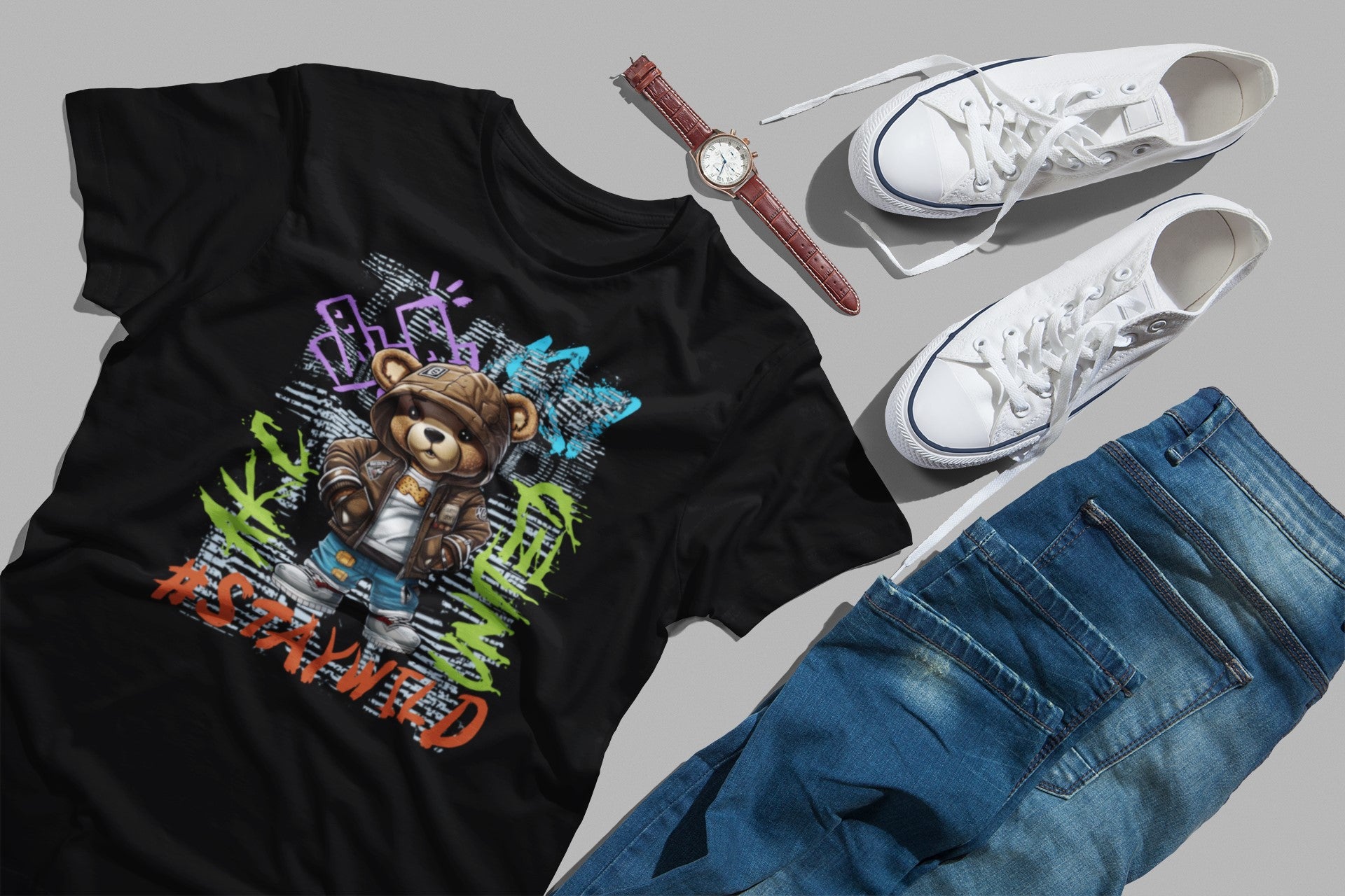 Black t-shirt with colorful graphic design, white sneakers, blue jeans, and a watch on a gray background