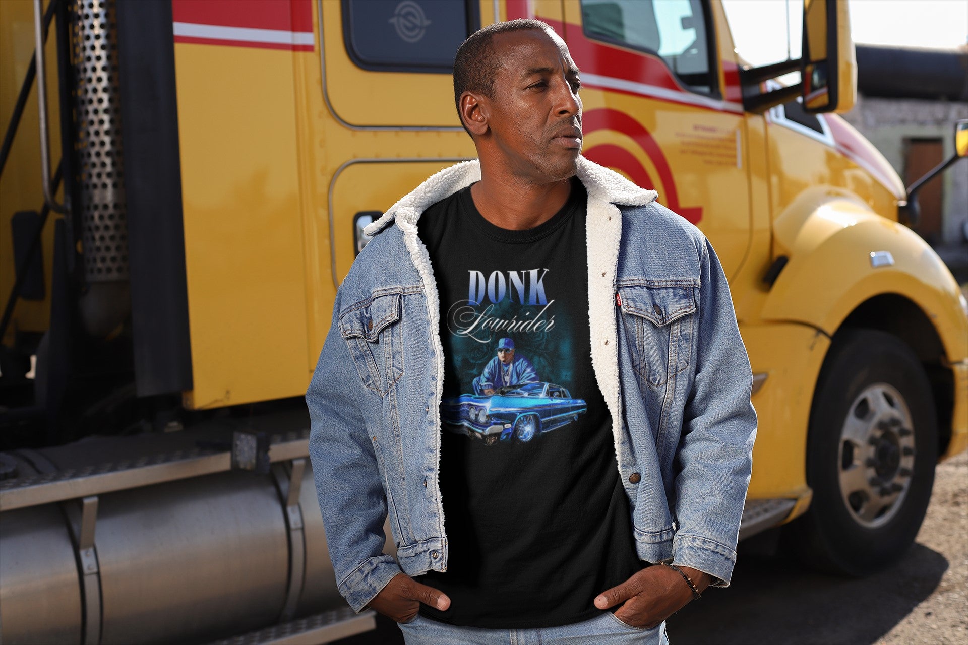 Man wearing a black t-shirt with graphic design and text, standing in front of a yellow truck.