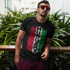 Man wearing a black t-shirt with Hungarian flag design and sunglasses, standing in front of green plants.