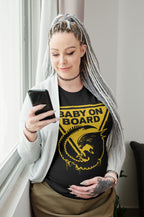 Woman wearing a black t-shirt with 'Baby on Board' graphic and holding a phone.