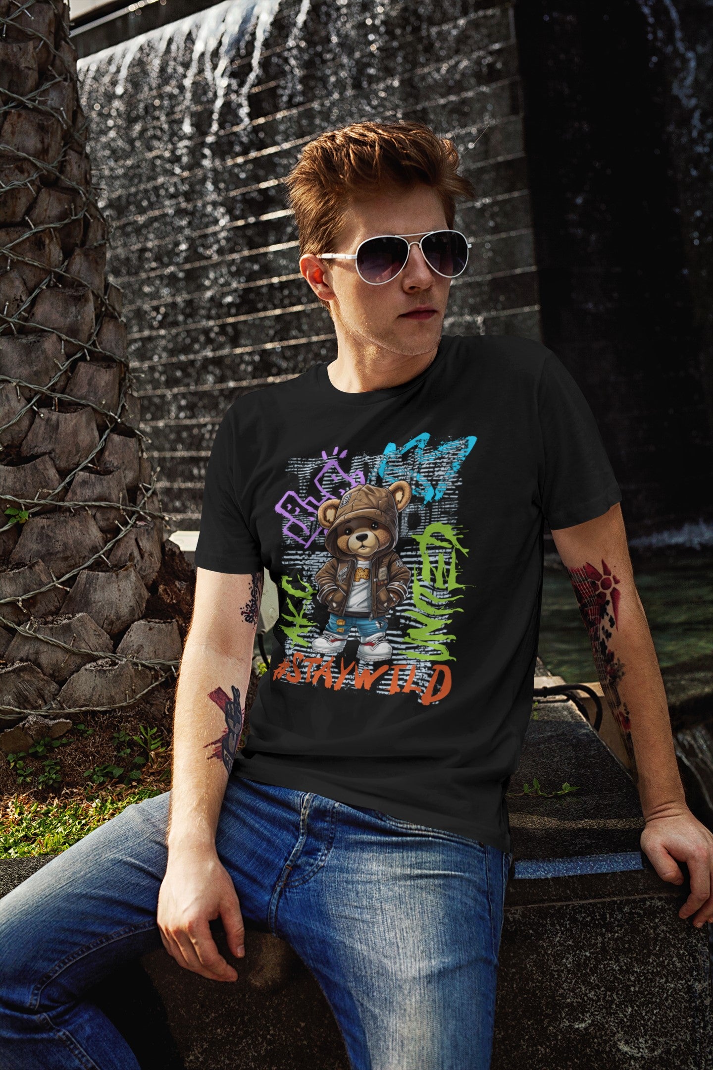 Person wearing a black t-shirt with colorful graphic design sitting in front of a water fountain.