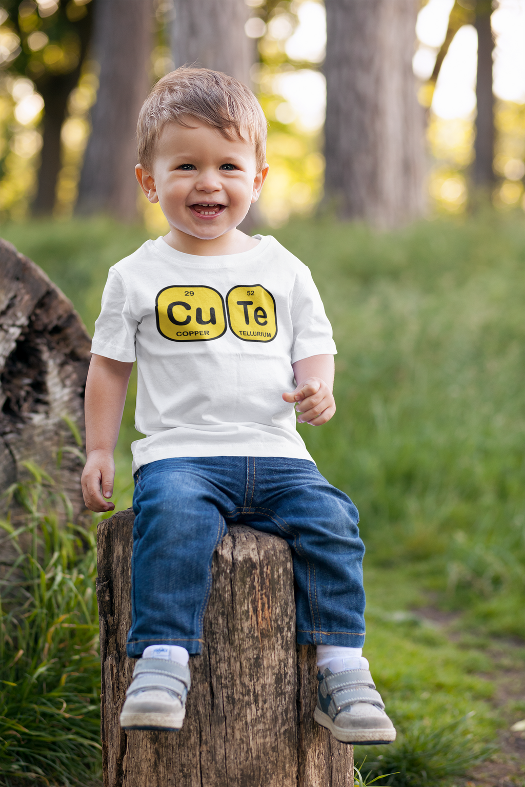 Child wearing a shirt with 'Cu Te' design sitting on a log in a forest