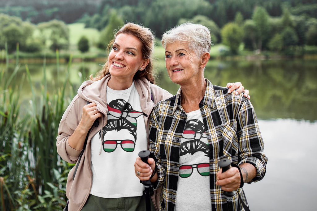 Two women walking outdoors by a lake, wearing matching t-shirts with sunglasses design.