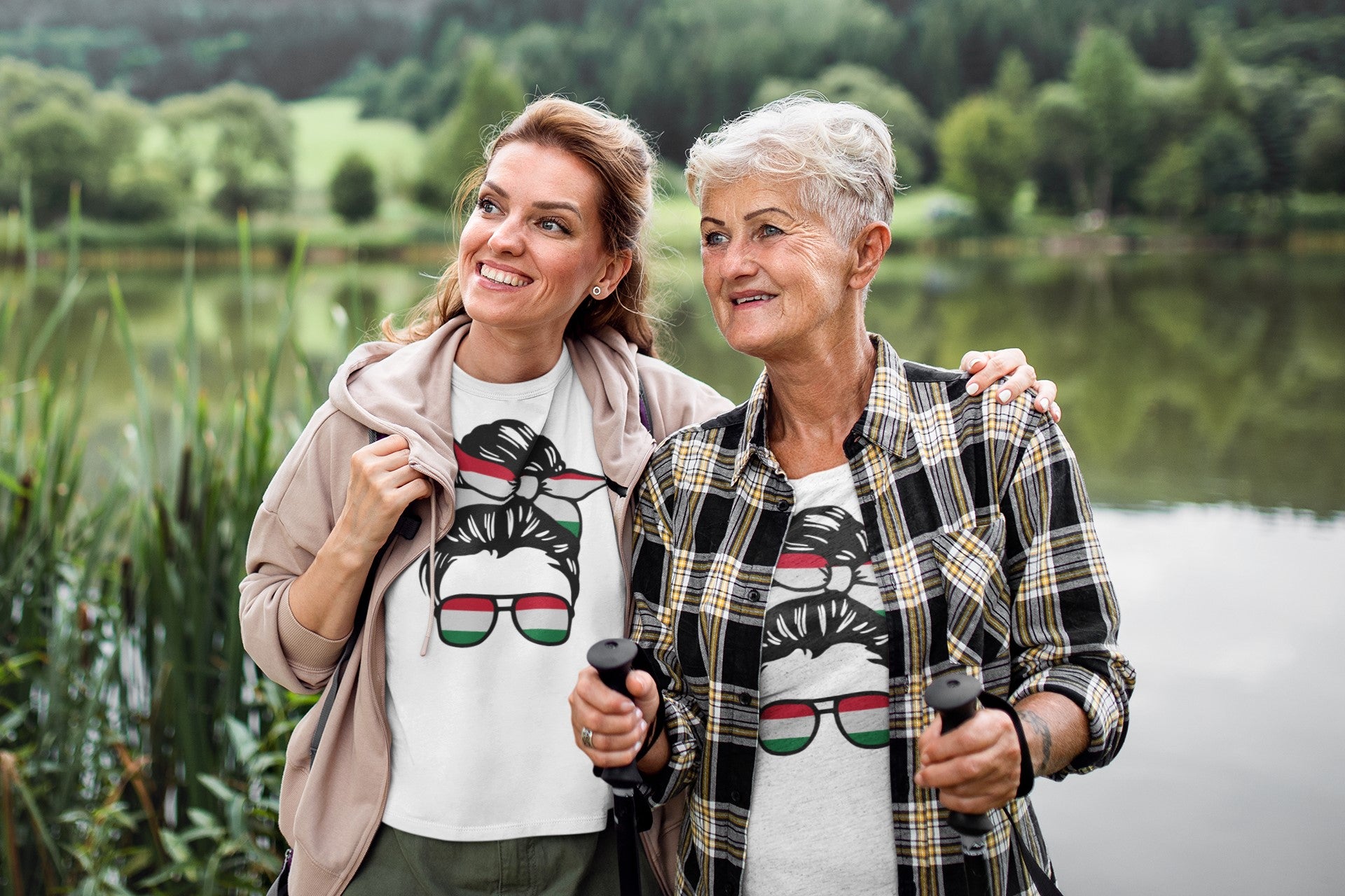 Two women walking outdoors by a lake, wearing matching t-shirts with sunglasses design.