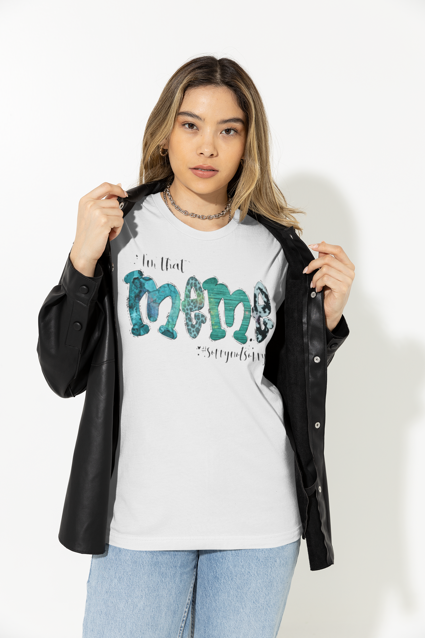A woman modeling a white graphic t-shirt with a black faux-leather jacket draped over her shoulders, paired with light blue jeans, against a plain white studio background.