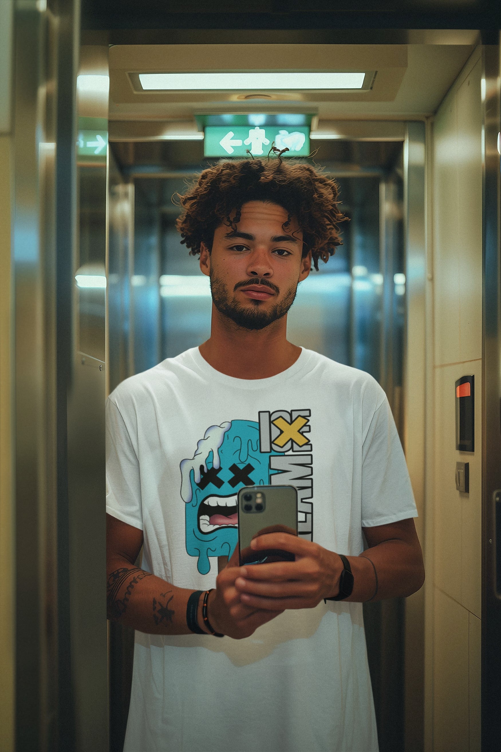 Man in a white t-shirt with a graphic design holding a phone in an elevator.