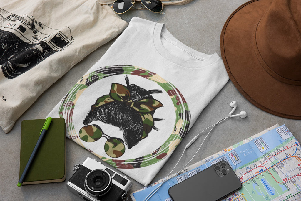 White t-shirt with a black bear design on a gray surface with accessories like a hat, camera, and map.