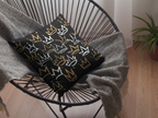 Decorative pillow with crown pattern on a black wire chair with a gray blanket.