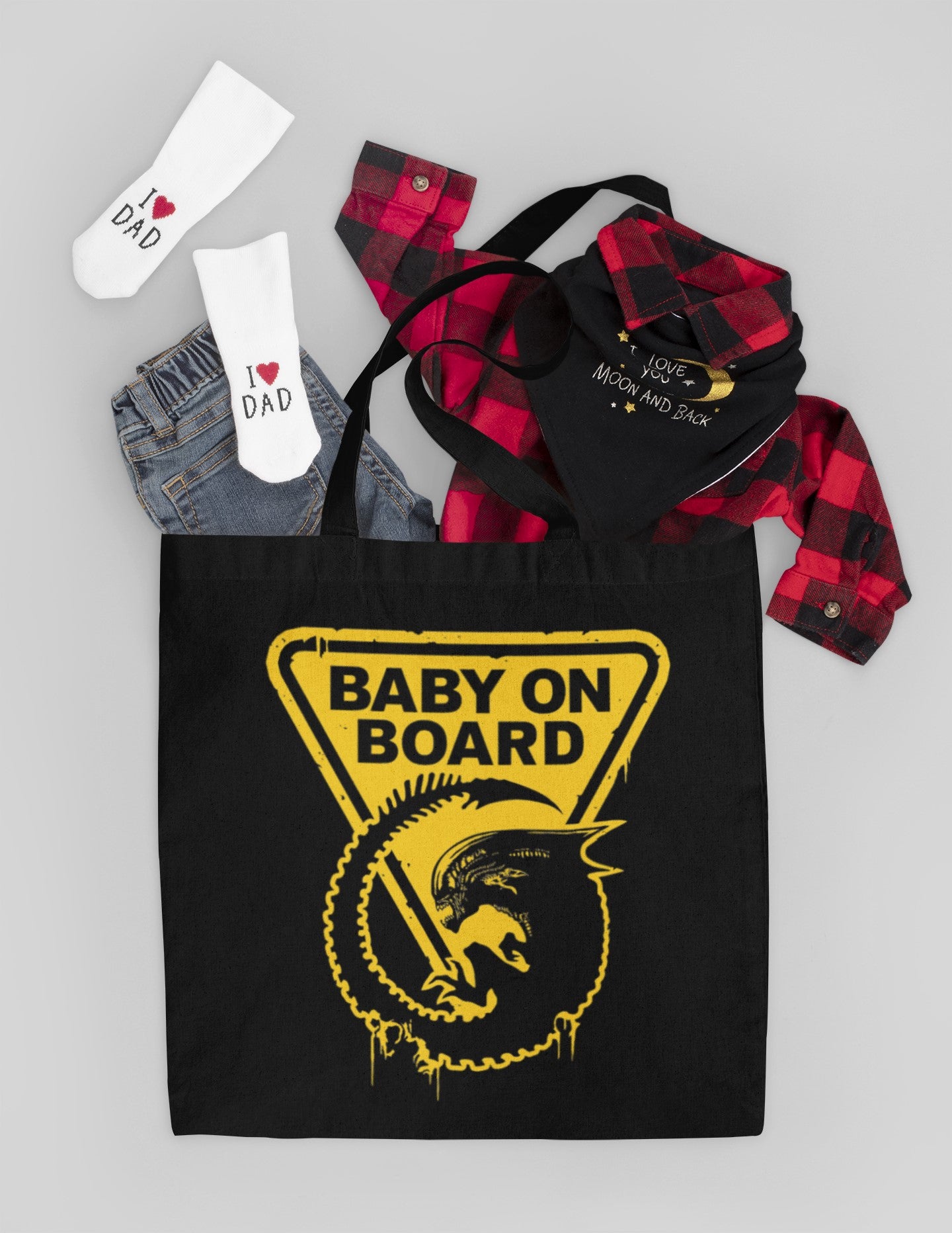 Black tote bag with 'Baby on Board' graphic, red plaid shirt, denim jeans, and white socks on a light gray background.