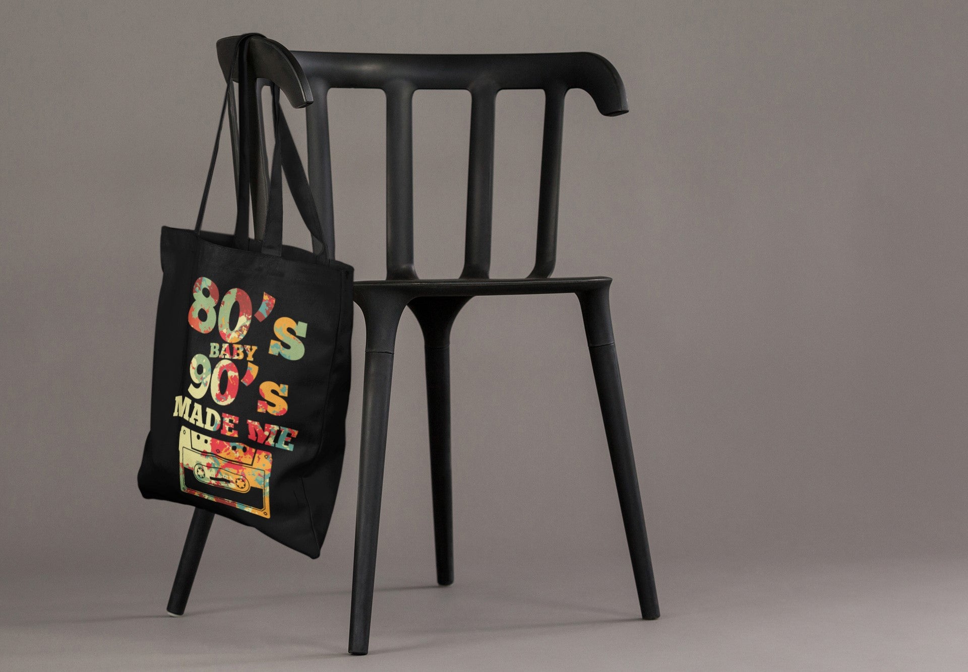 Black tote bag with colorful text and graphics hanging on a black chair against a gray background
