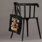Black tote bag with colorful text and graphics hanging on a black chair against a gray background