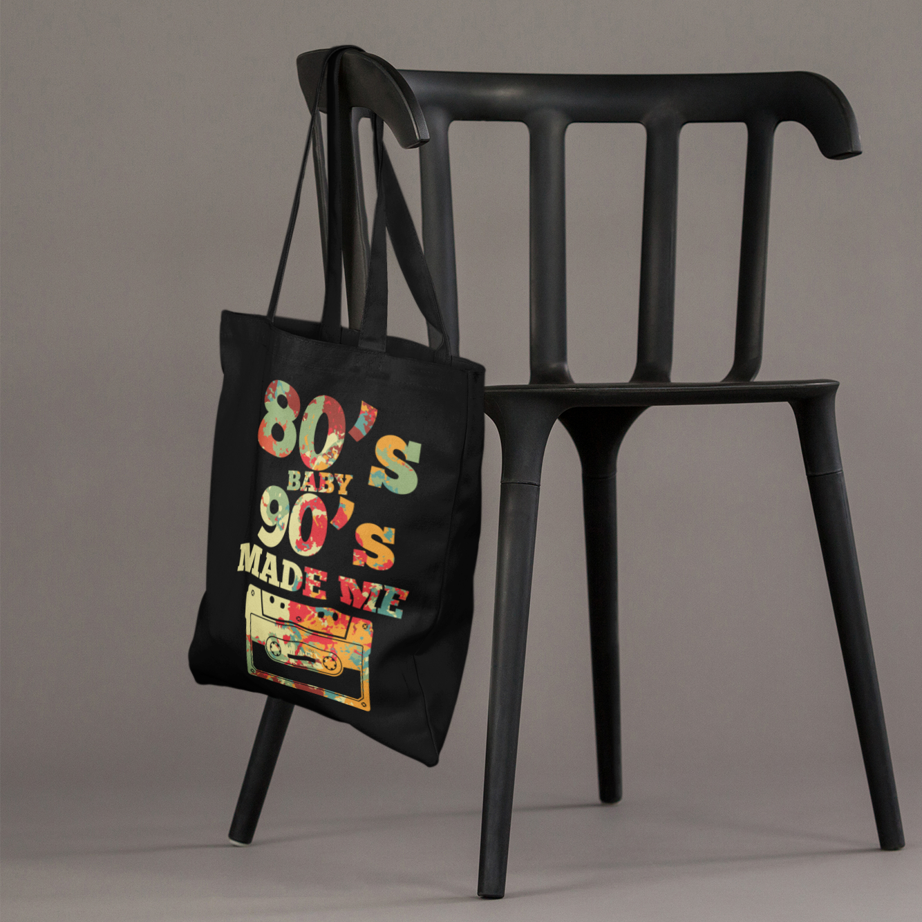 Black tote bag with colorful text and graphics hanging on a black chair against a gray background