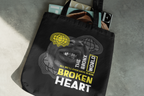 Black tote bag with graphic design and text on a concrete surface