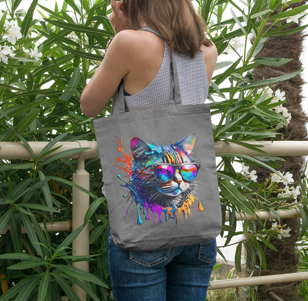 Person holding a tote bag with a colorful cat design in front of green foliage