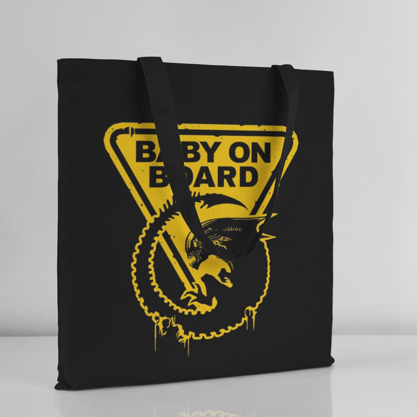 Black tote bag with yellow 'Baby on Board' graphic on a light gray background