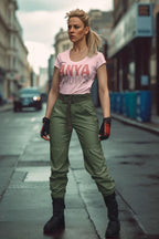 Woman in a pink t-shirt and green pants standing on a city street.