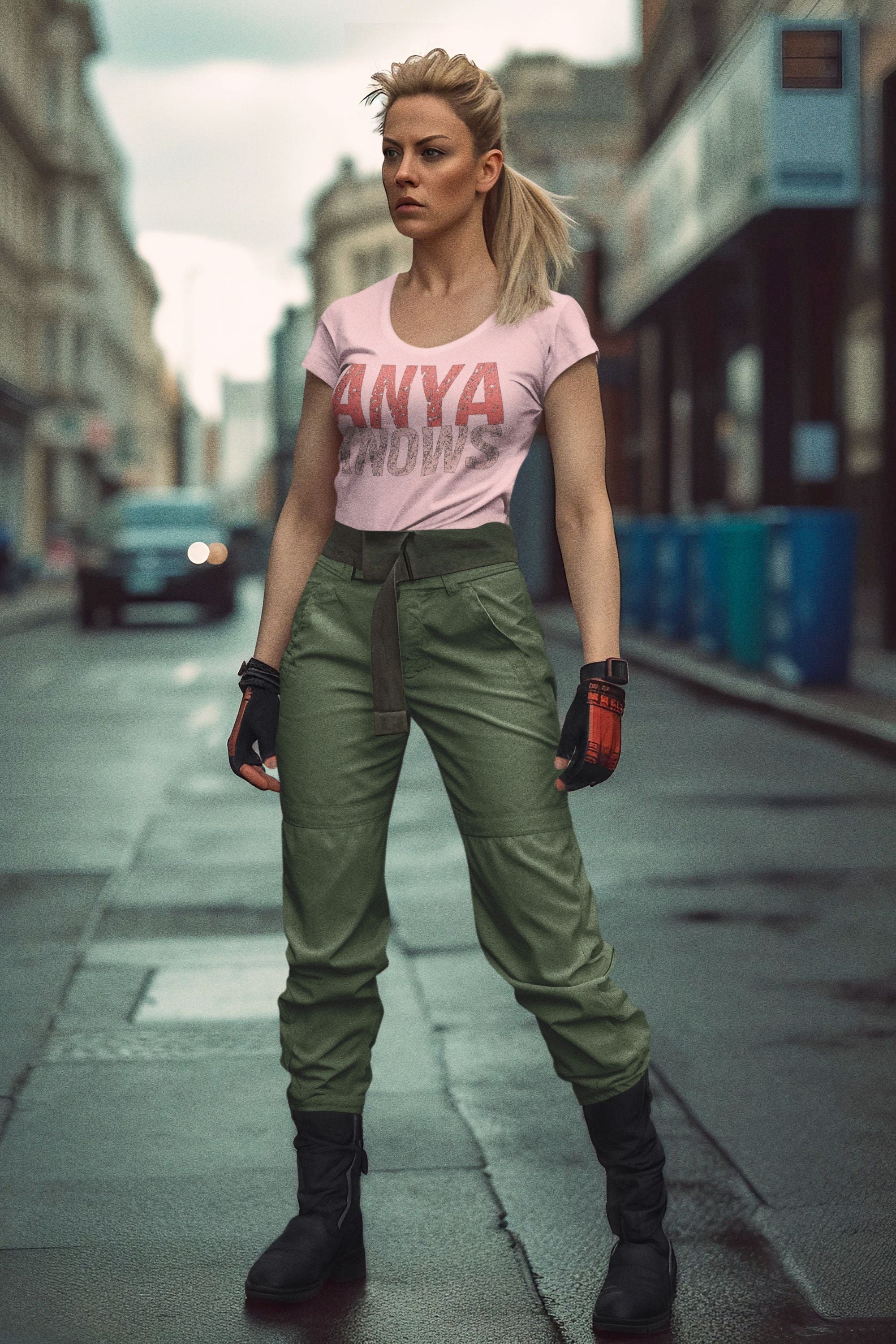 Woman in a pink t-shirt and green pants standing on a city street.